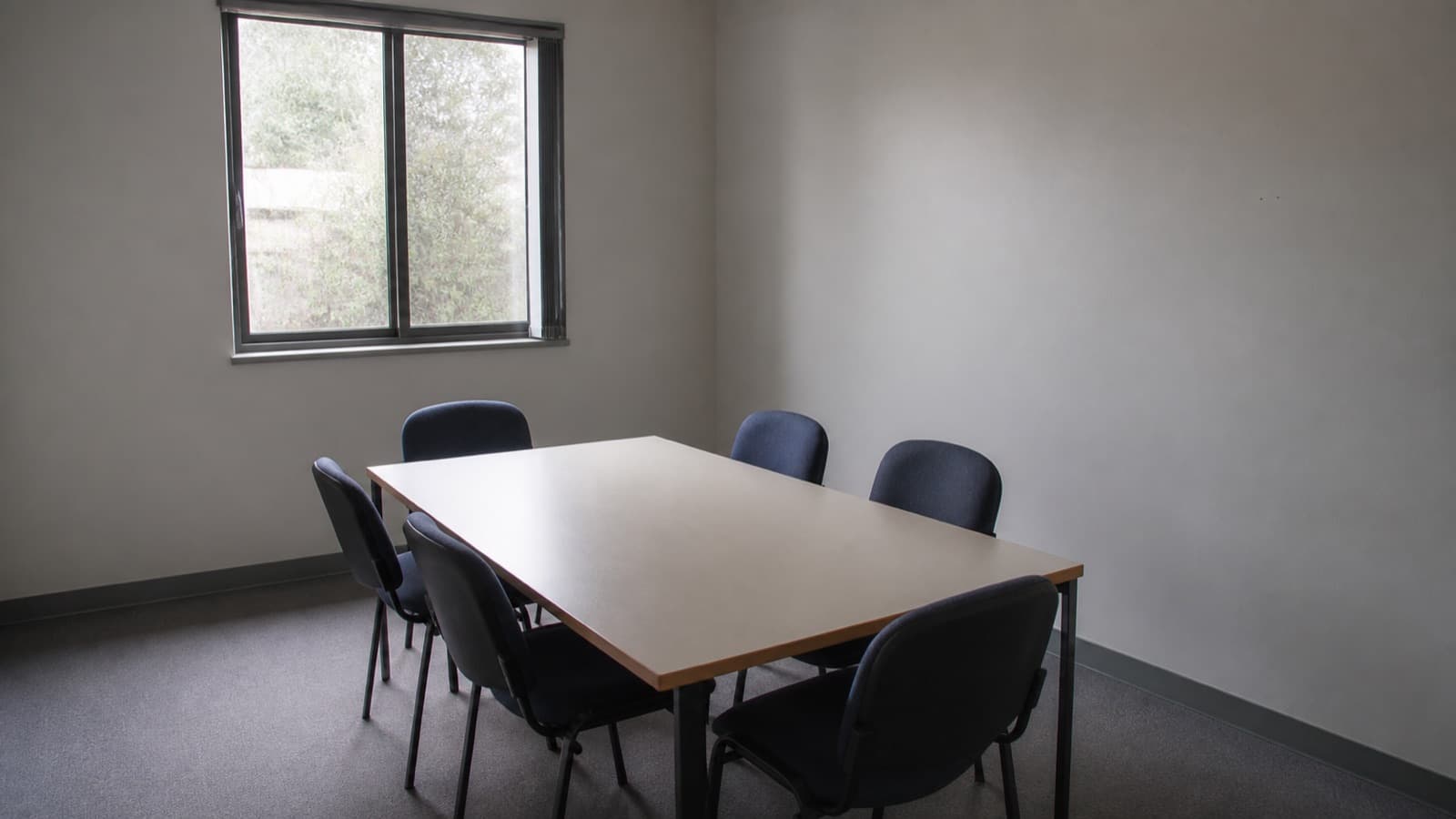 A small, plain, empty meeting room with daylight through a window.